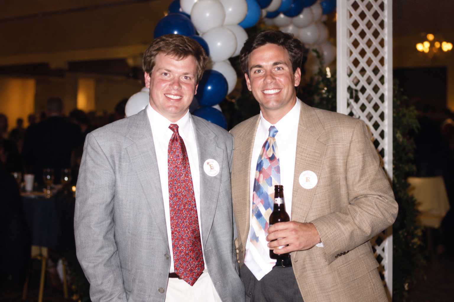 Two men in suits pose beneath the balloon arch. Color interpretation.
