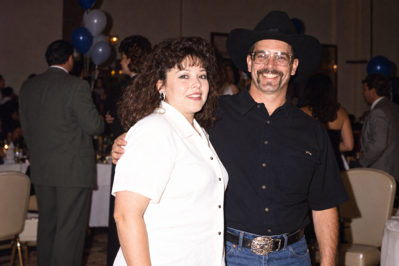 A woman and a man stand together with his arm around her. Color interpretation.