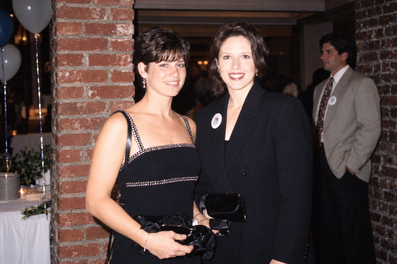 Two women pose together in front of a brick wall. Color interpretation.